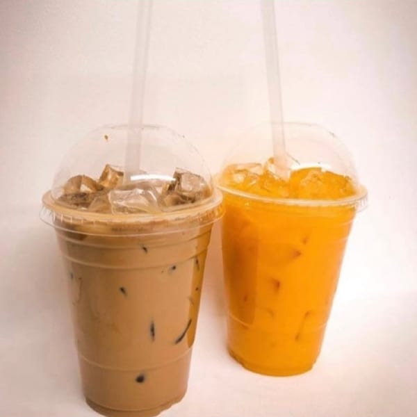 Two iced drinks, one brown and one orange, in clear plastic cups with domed lids and straws.