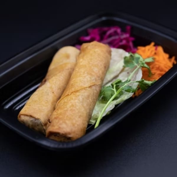 Two crispy Pho Go spring rolls with shredded carrots, purple cabbage, and lettuce in a black container.