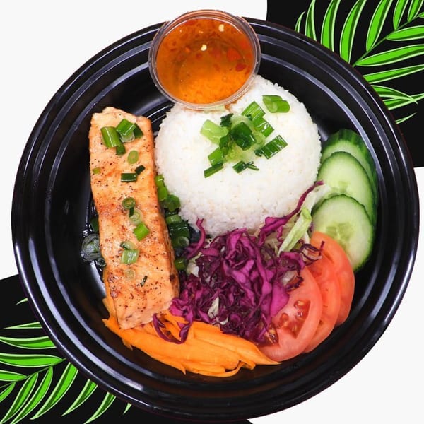Grilled salmon with rice, sliced cucumbers, tomatoes, shredded carrots, purple cabbage, and sauce.