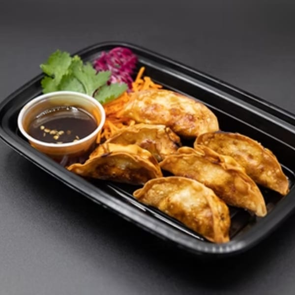 Golden-brown fried dumplings, with a side of dipping sauce, shredded carrots, and cilantro in a black container.